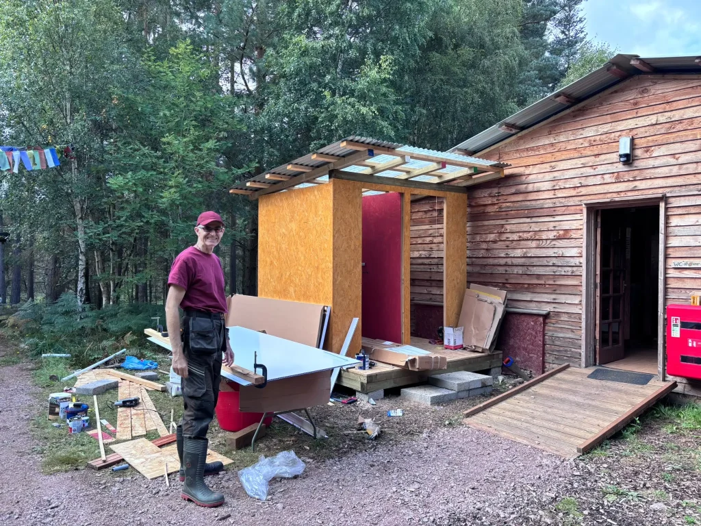 DIY maintenance volunteer smiling in front of shower and toilet block.