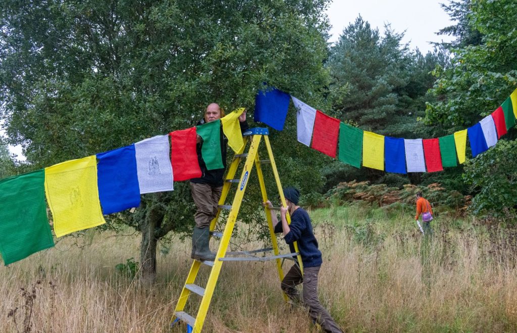 International volunteers hanging prayer flags in the trees at Buddhist Centre Scotland.